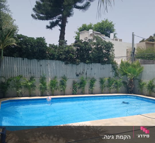 בריכה מוקפת בצמחייה וגדר עץ